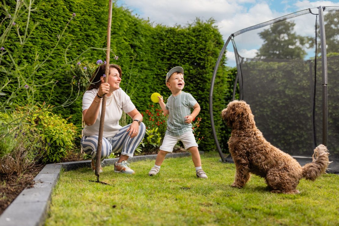 Vrouw en kind spelen met een hond in een groene tuin